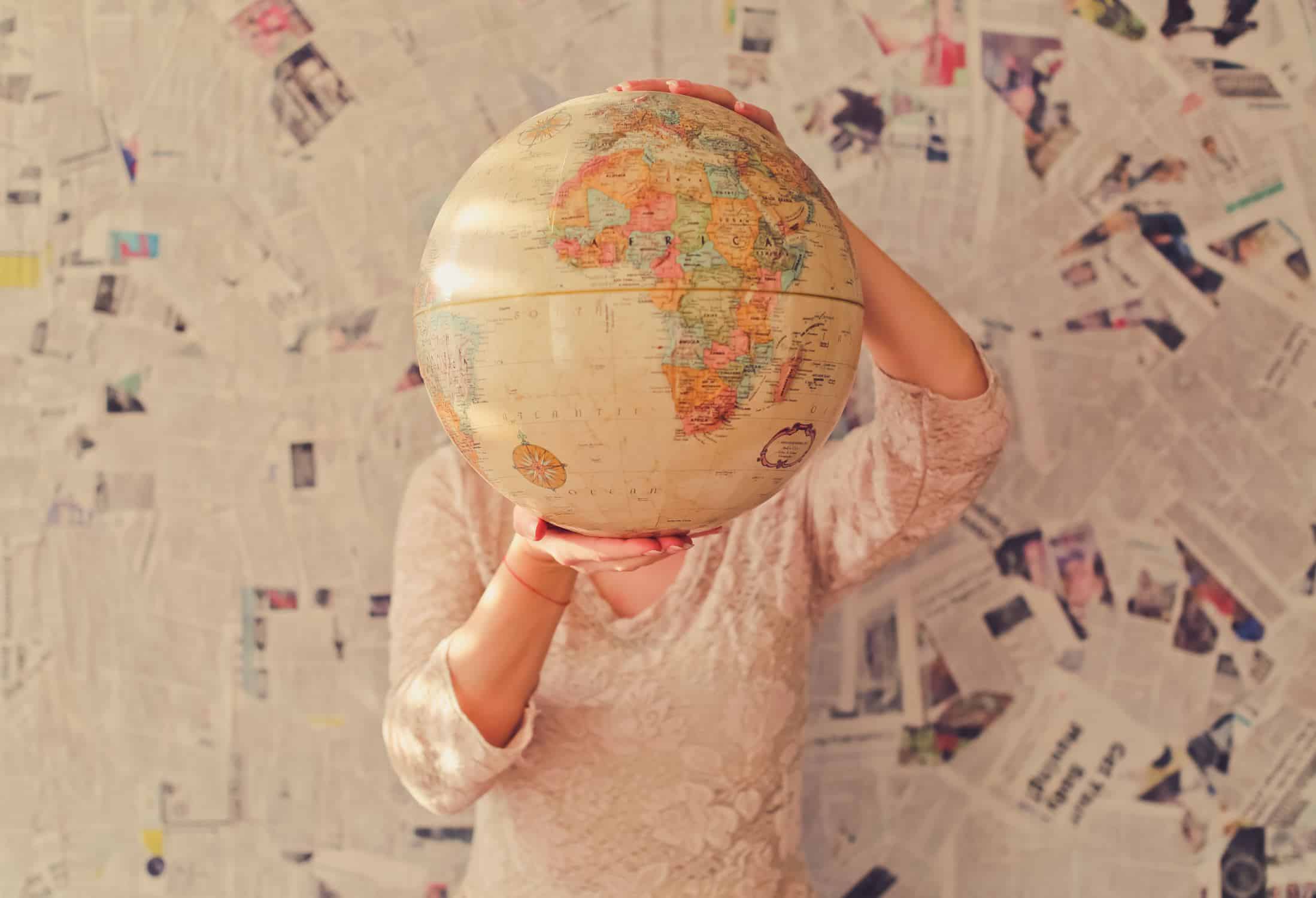 Woman holding a globe in front of her face with newspapers behind her