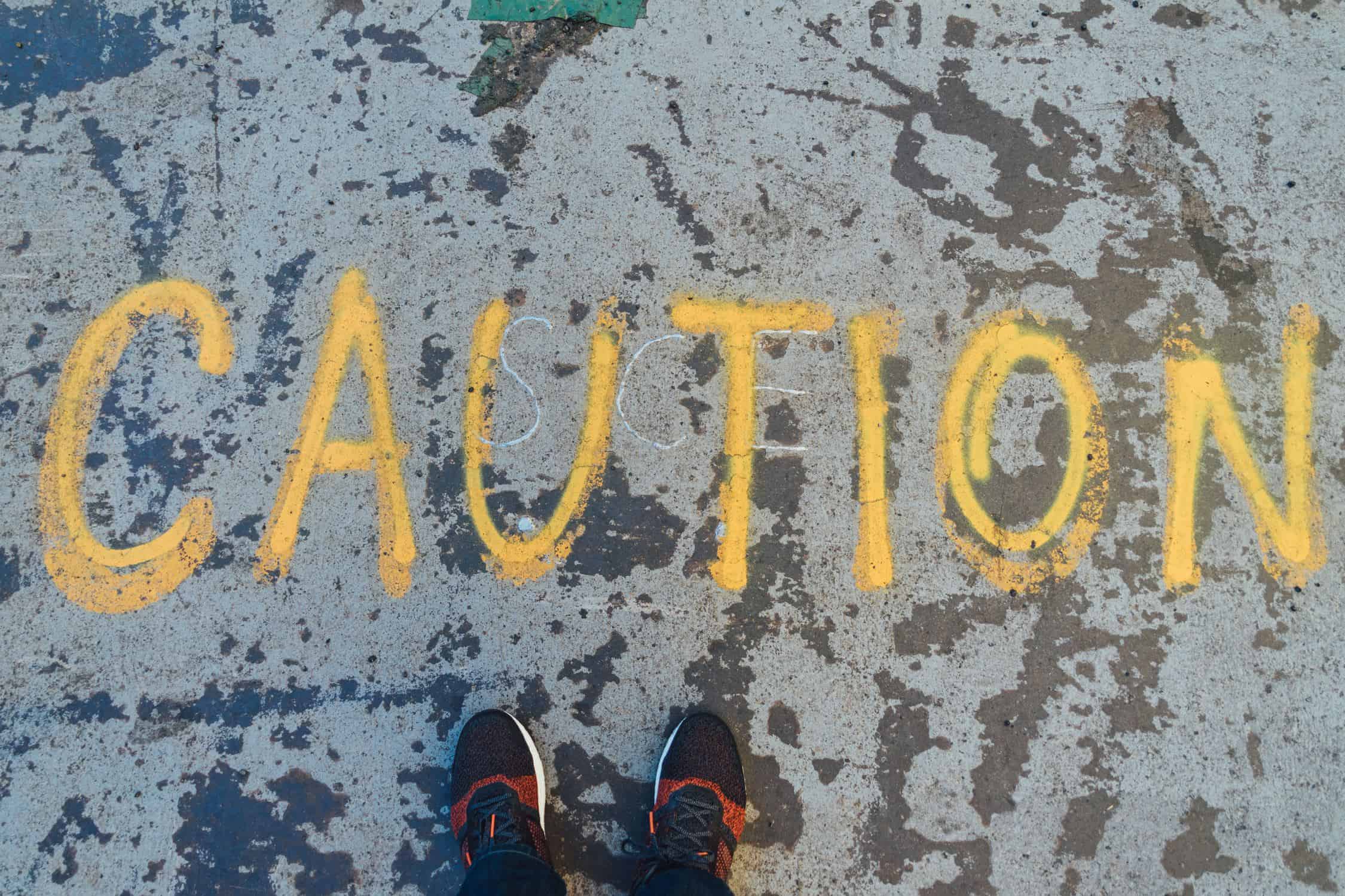 Caution written on the ground. Perspective from above. Shoes standing beside "caution"